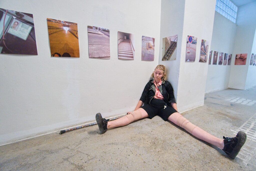 Fotka Eri, který sedí na zemi před svou instalací fotek z úhlu pohledu vozíčkářstva.