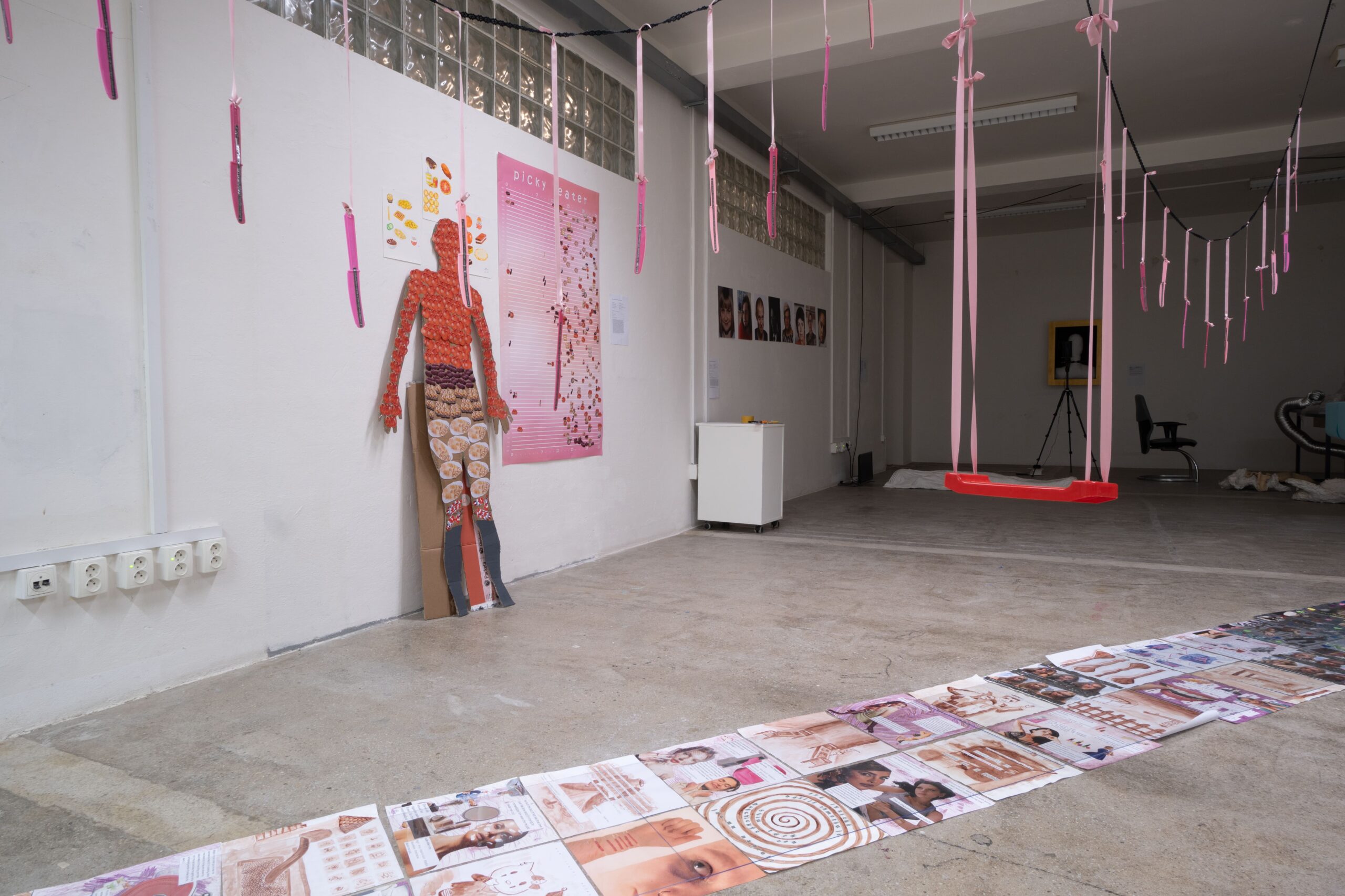 chodník z barevných koláží nad kterými visí na stuhách růžové nože a červená houpačka